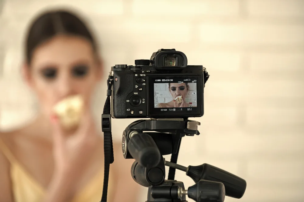 Camera back side with image of girl on screen display. Woman model eat apple on white wall. Nutrition, healthy lifestyle, health, diet concept. Photography, focus, exposure, techno
